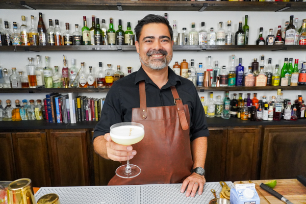 Bartender holding a 5-ingredient Pisco Sour with a dash of bitters in a cocktail glass