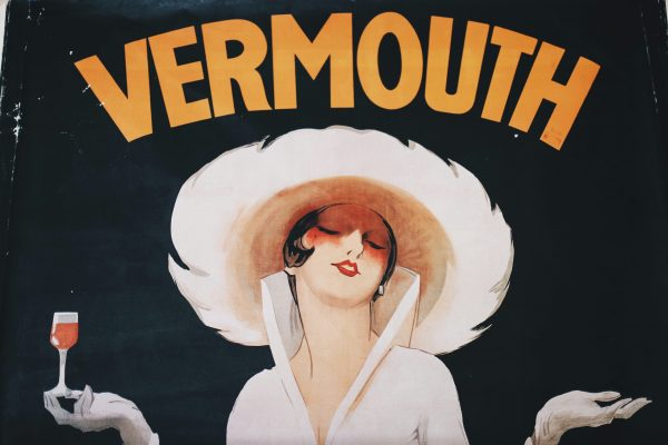 Old cartoon poster for vermouth with a woman in all white and a fancy feather hat holding a cocktail, with the word 