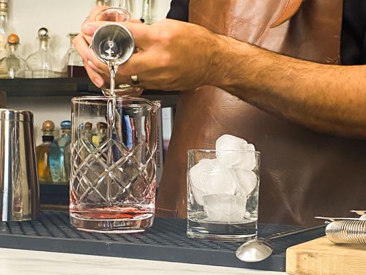 Pouring a cognac and base of rye whiskey mixture into a mixing glass