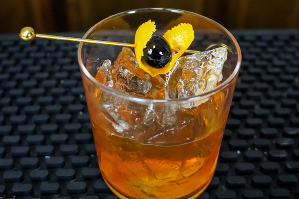 an old fashioned bulleit bourbon cocktail with orange peel and maraschino cherry and 2 ounces bourbon