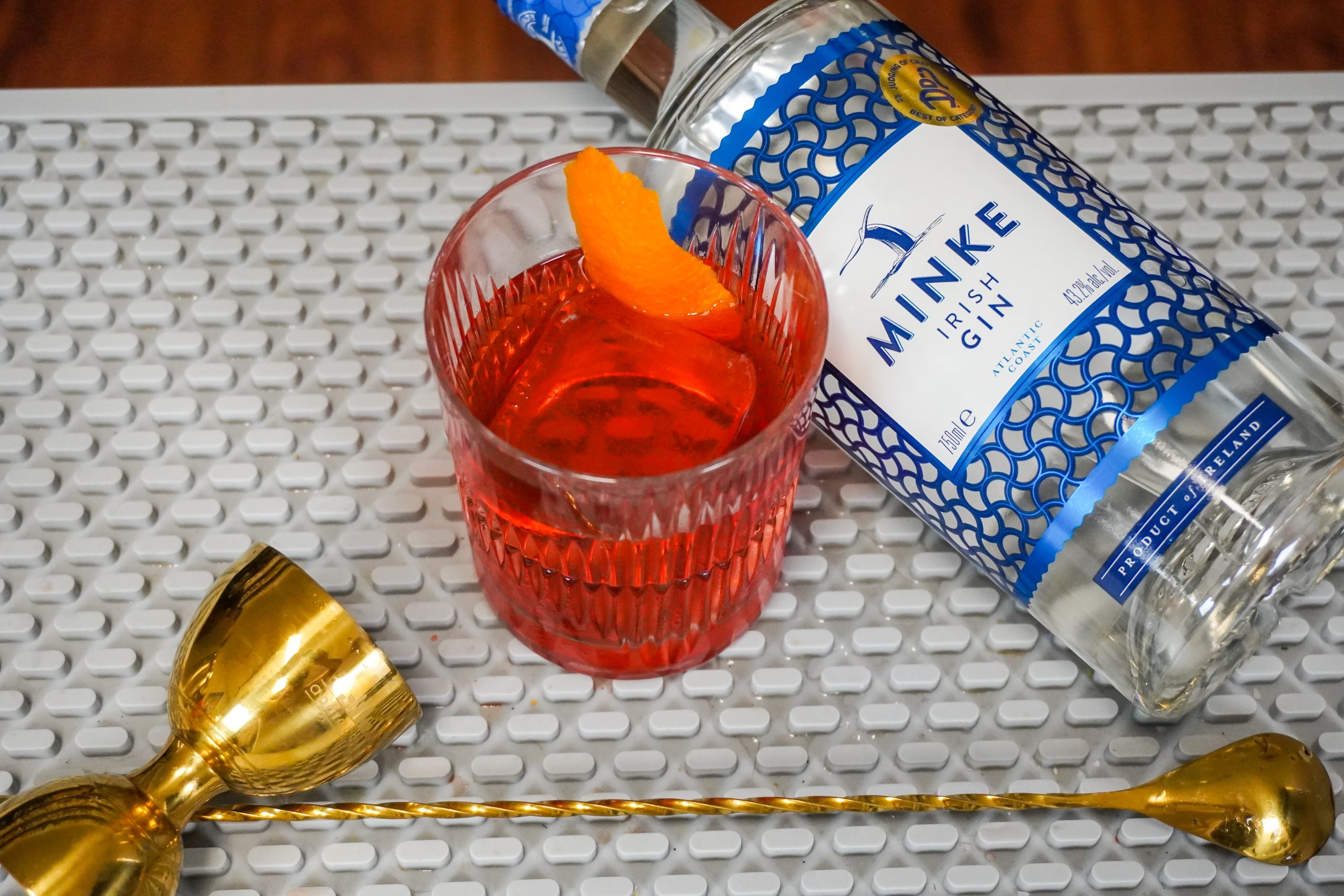 Negroni, a favorite cocktail, with orange garnish and fortified wine, a cocktail jigger, and bar spoon
