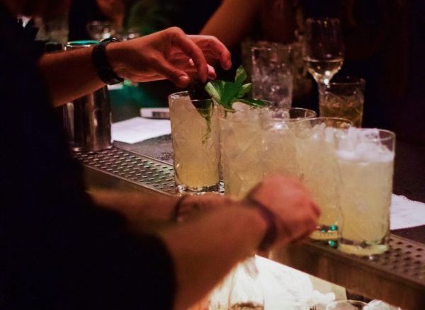 the hands of a bartender behind a bar making 5 drinks in tall glasses