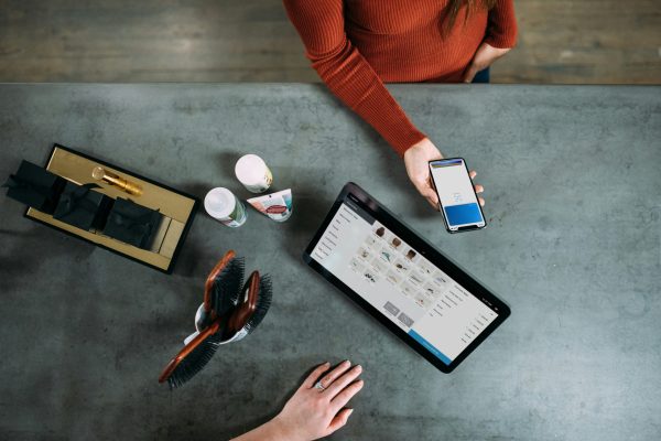 the hand of a customer holding a phone to pay into a business' computer systerm