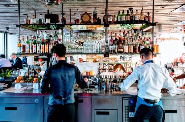 2 bartenders from behind, in front of a fully-stocked bar