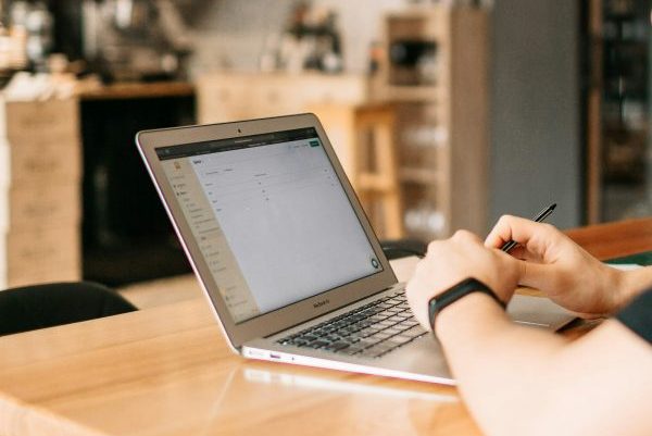 a laptop on a restaurant table with hands at it and a bar in the background