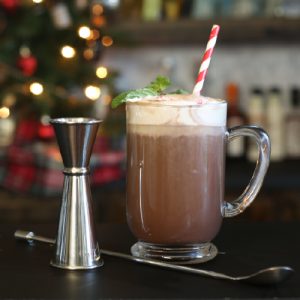 Spiked hot chocolate in a glass mug with peppermint and a cocktail jigger