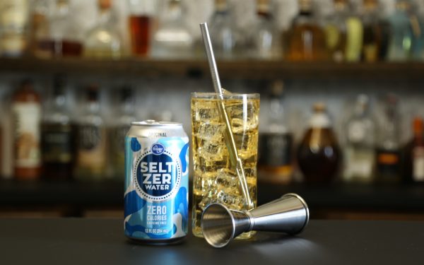 Whiskey cocktail with cocktail jigger and can of seltzer water on a bar