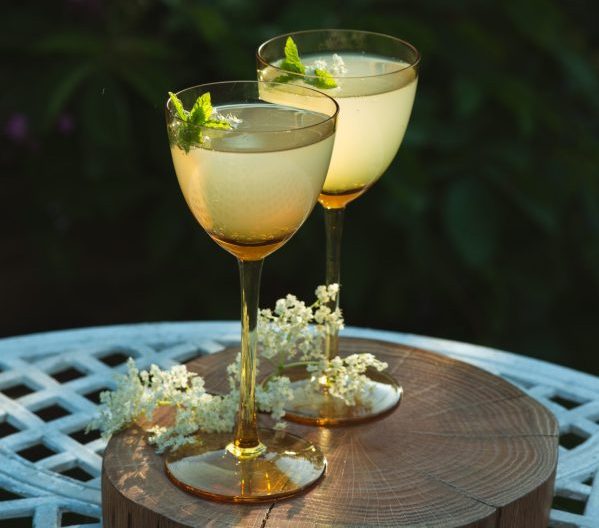 2 cocktails on a wooded round platter with babies breath flowers and mint by margaret-jaszowska via unsplash