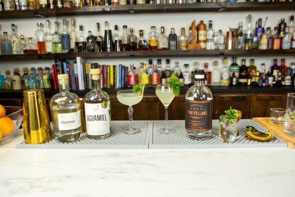 two versions of the southside cocktail surrounded by ingredients, barware, and liquor bottles on a bar
