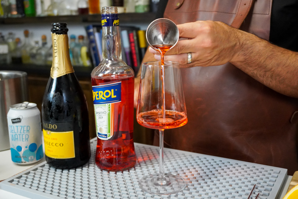Bartender making a pre-dinner drink with bottle of prosecco italian wine and aperol for citrus flavor