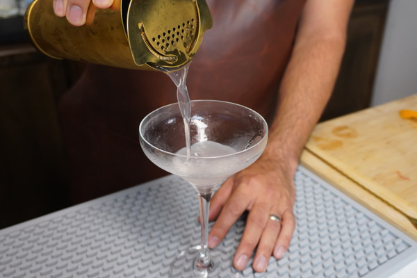 head bartender pouring a cosmopolitan into a coupe cocktail glass