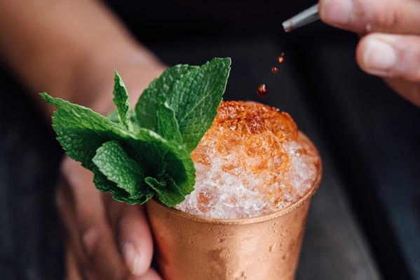 aromatic bitters being squeezed by a head bartender into a copper mug with fresh mint leaves by adam jaime via unsplash