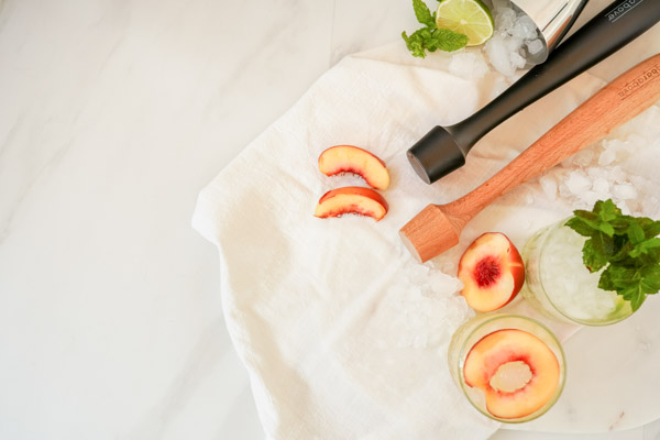 cocktail muddlers with peaches and fresh mint leaves