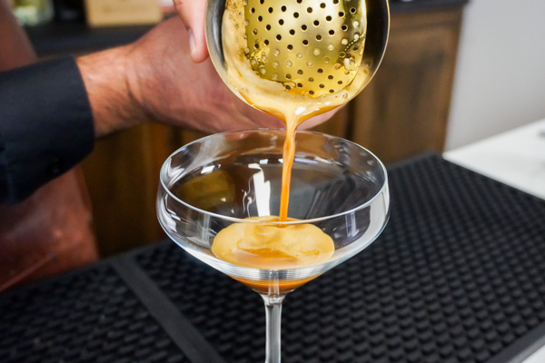 Pouring the cocktail into a chilled glass to create a gorgeous foam layer