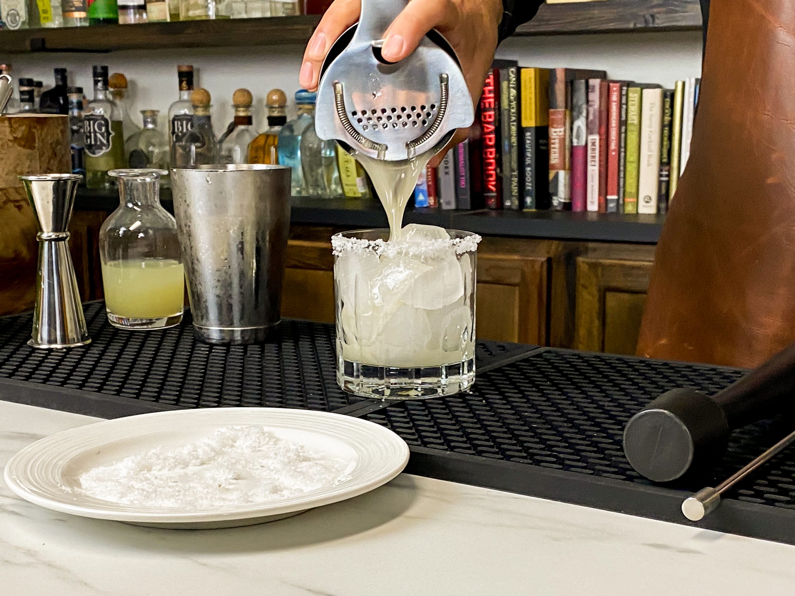 Pouring home margarita mix with citrusy flavor into a glass with salt
