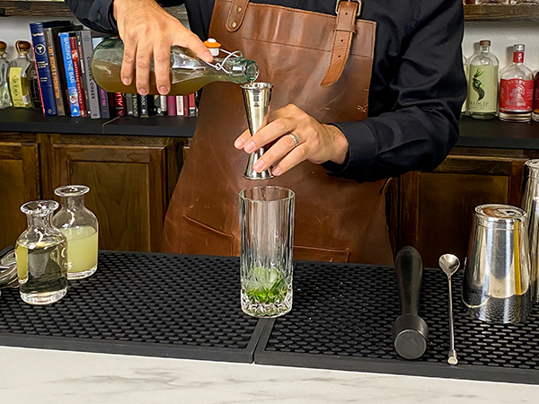 Pouring non-alcoholic rum with a tall glass with iceand extra mint with 1 tbsp lime juice
