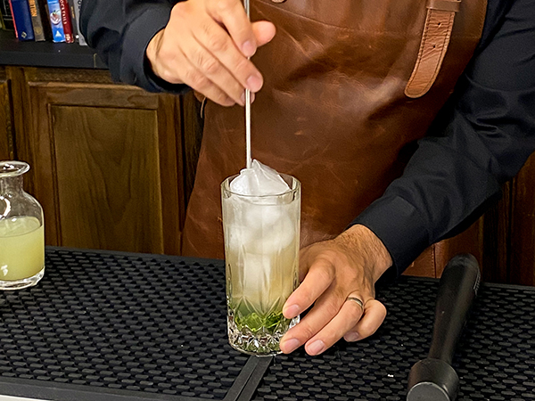 Stirring mojito ingredients in elegant highball glasses, which are crystal glasses
