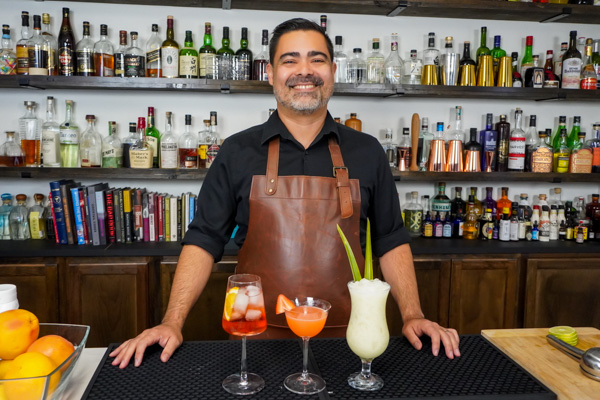 bartender with three fun drinks, including 2 tropical drinks on a bar
