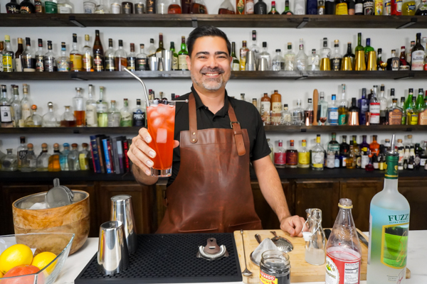 Bartender holding a pink coloured drink with cherry syrup in a cocktail glass