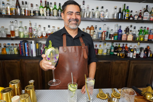 Bartender with a tall glass, holding a classic drink with citrus fruit