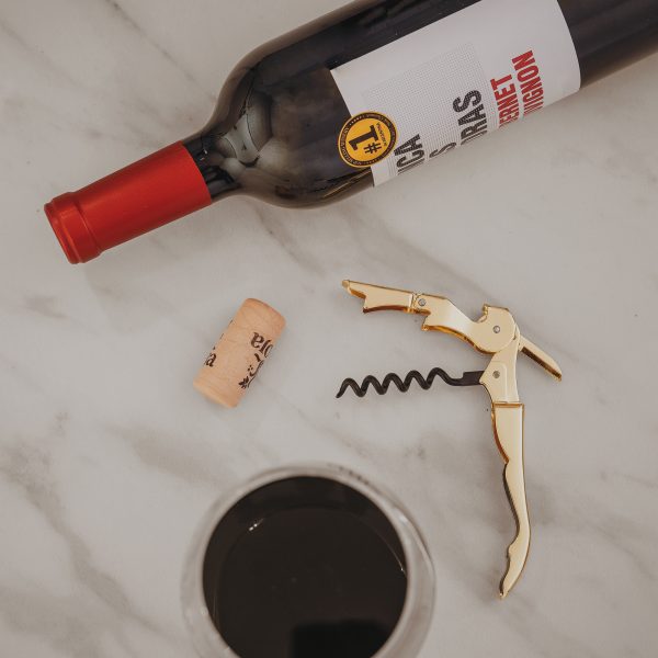 gold wine bottle opener with a delicate cork, sitting next to a glass of wine and a wine bottle