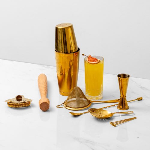 14 piece bar set in gold with an orange cocktail in a tall glass