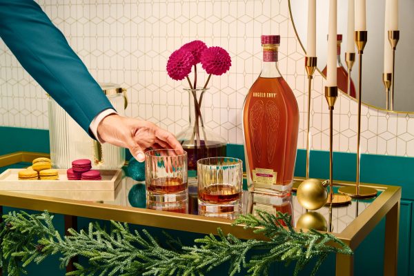 hand reaching for a rocks glass of whiskey next to a bottle of bourbon on a bar tray