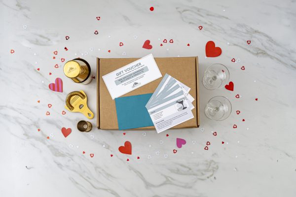romantic date night ideas for couples: cocktail gift box with shaker, strainer, jigger, glasses, course, recipes, all surrounded by paper hearts