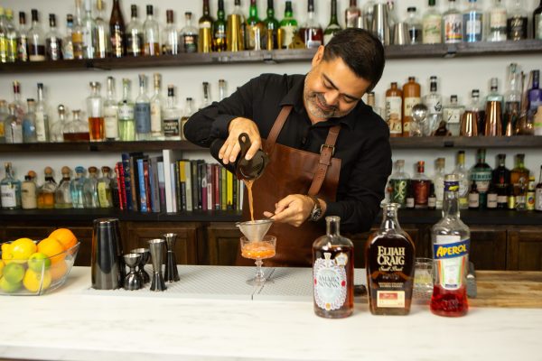 bartender pouring a cocktail through a fine mesh strainer