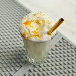 Creamy cocktail with orange zest and a gold straw