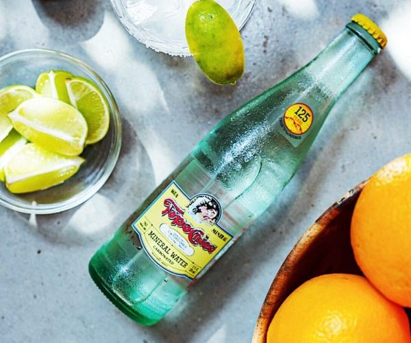 Bottle of Topo Chico water next to drink with ice and extra lime slices