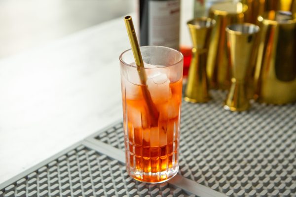 Americano a red cocktail in a tall glass with ice and a gold straw