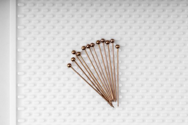 a dozen antique copper bronze cocktail picks on a white silicone bar mat